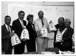 black and white photo of adults holding bags with dollar signs on them.