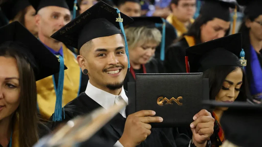 CMC 2023 graduate smiling and holding up their diploma in the audience