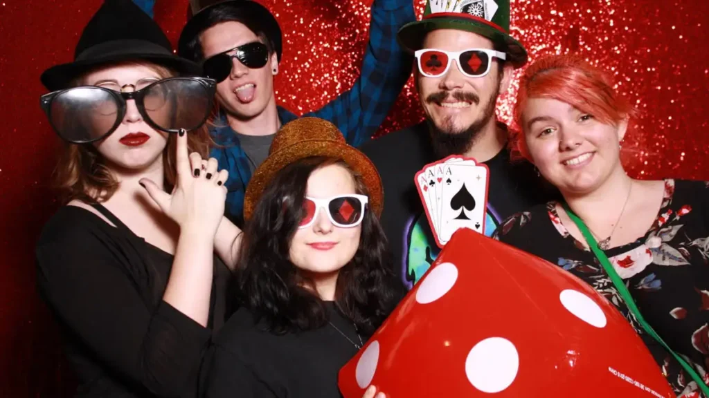 students wearing casino card glasses, holding dice, and posing in front of a sparkly red background