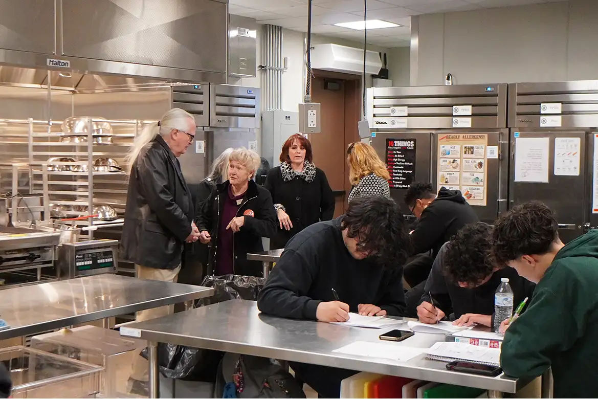 students taking notes in the kitchen and board members observing