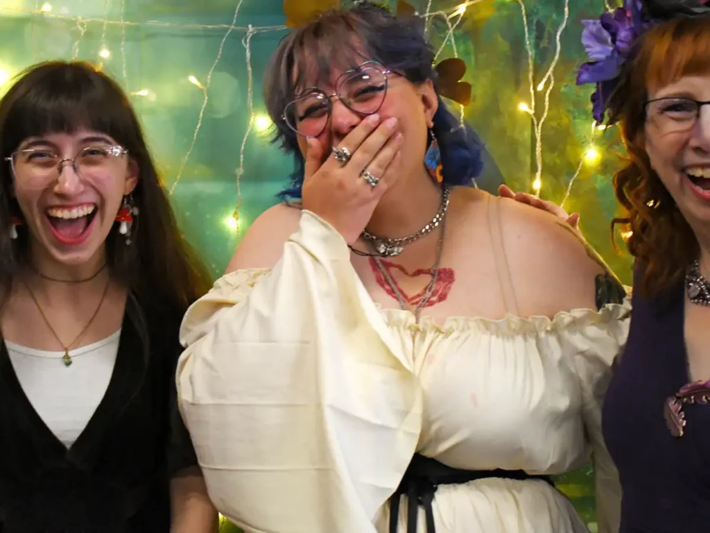 3 female students smiling and laughing together in front of a green backdrop with curtain lights