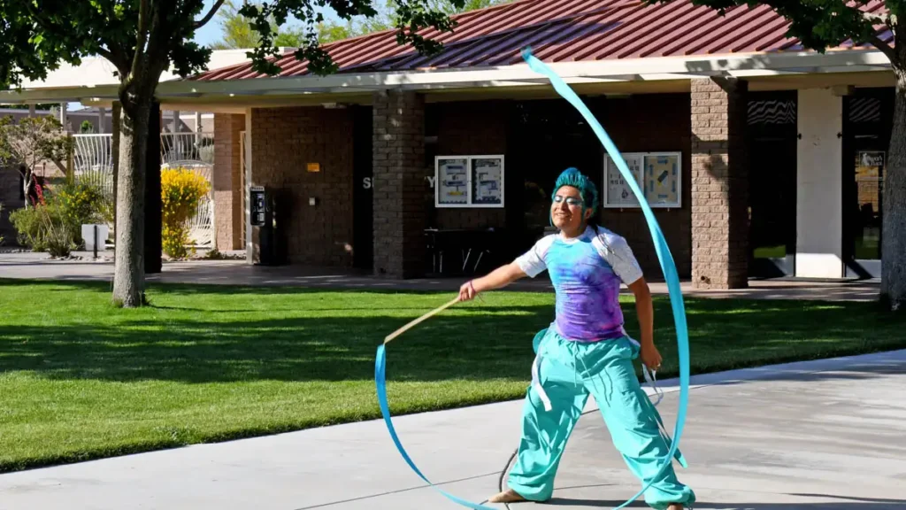 student wearing a pink, purple and blue tie dye t-shirt, bright blue-green pants performing a rhythmic routine in the quad