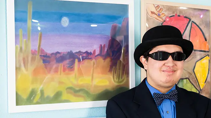 student in bowler hat and glasses standing in front of artwork