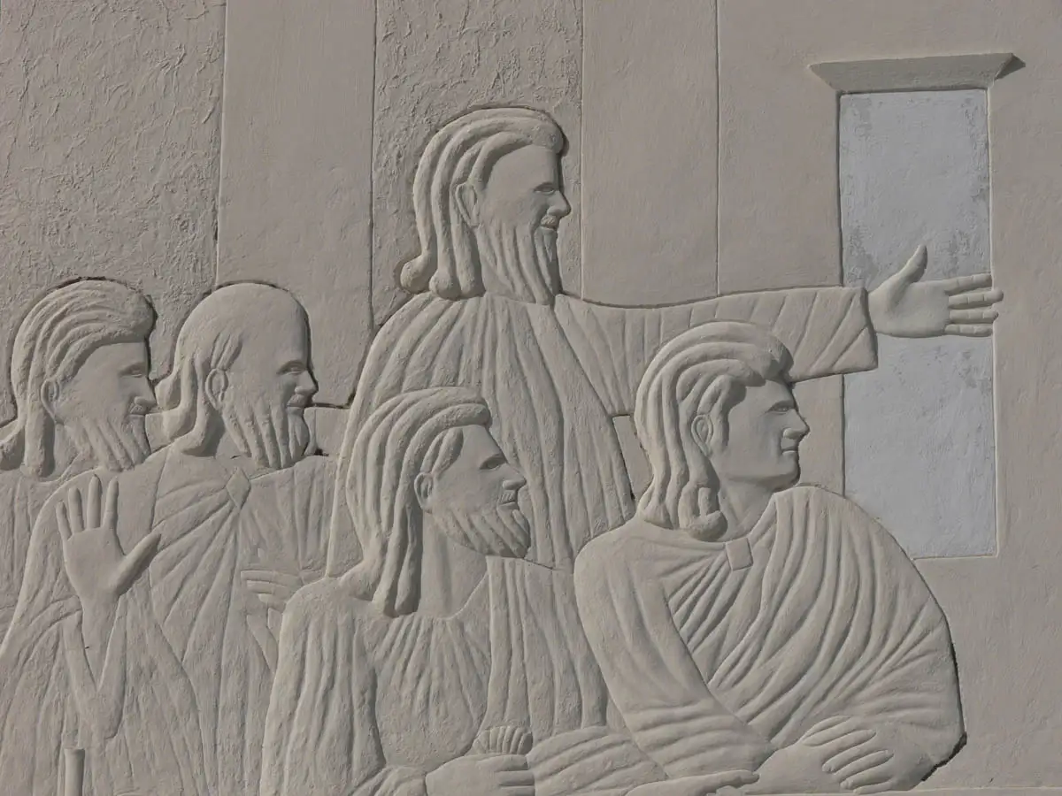 carving of 4 men in robes turning their heads to the side in a white clay-like material